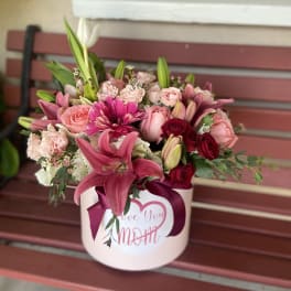 Pink and red mixed flower arrangement in a round box with a ribbon