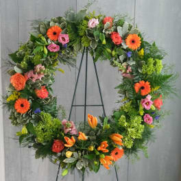Large floral wreath with orange, pink, and green flowers on a black stand