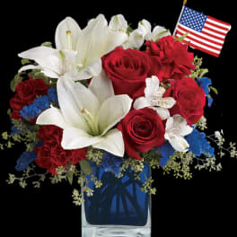 Red roses and white lilies in a blue vase with a small American flag