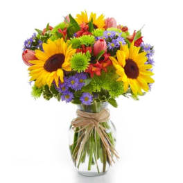 Mixed bouquet of sunflowers, tulips, and purple daisies in a glass vase