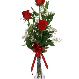 Three red roses in a clear glass vase with a red ribbon
