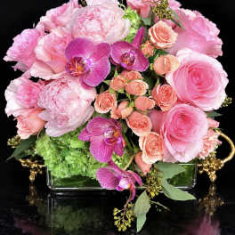 Pink roses and orchids arranged in a glass vase with green hydrangea
