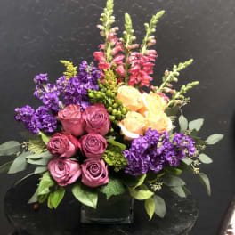 Bouquet of pink and peach roses with purple flowers in a glass vase