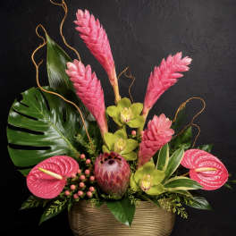 Tropical arrangement with pink blooms and green orchids in a gold vase