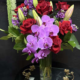 Bouquet of red roses, purple orchids, and lilies in a glass vase