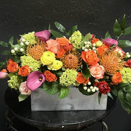 Colorful floral arrangement in a gray rectangular box with pink calla lilies and roses