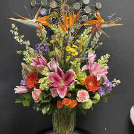 Tall mixed bouquet in a glass vase with pink lilies, roses, and orange birds of paradise