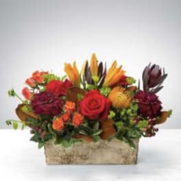 Mixed bouquet with red, orange, and burgundy flowers in a rectangular container