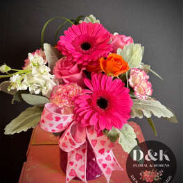 Pink gerbera daisies and roses in a purple vase with a heart ribbon