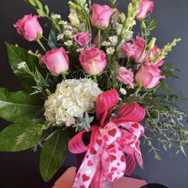 Pink roses and white hydrangea in a glass vase with heart ribbons