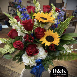 Bouquet of red roses, sunflowers, and white hydrangeas in a glass vase