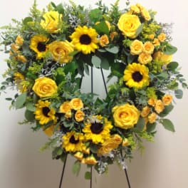 Yellow roses and sunflowers arranged in a wreath on a stand