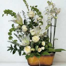 White roses and lilies arranged in a gold-toned container with orchids.