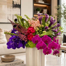 Large arrangement of purple orchids, calla lilies, and pink flowers in a white vase