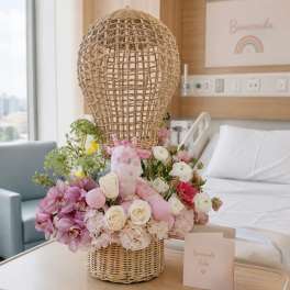 Pink and white floral arrangement with a plush giraffe in a wicker basket