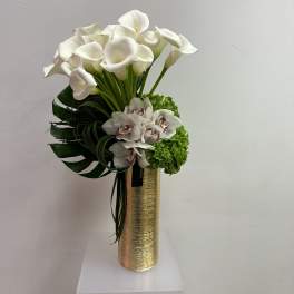 Tall gold vase with white calla lilies, green hydrangea, and white orchids in a modern arrangement