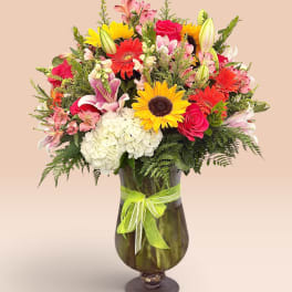 Mixed bouquet of roses, lilies, sunflowers, and gerbera daisies in a glass vase