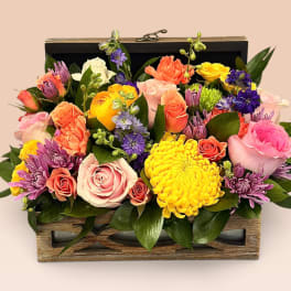 Mixed bouquet in a wooden box with pink, yellow, purple, and coral blooms