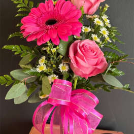 Pink roses and a hot pink gerbera daisy in a glass vase with a ribbon