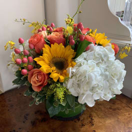 Mixed bouquet with sunflowers, coral roses, white hydrangea, and pink buds in a green vase