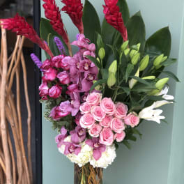 Tall bouquet of pink roses, orchids, lilies, and red tropical blooms in a glass vase.