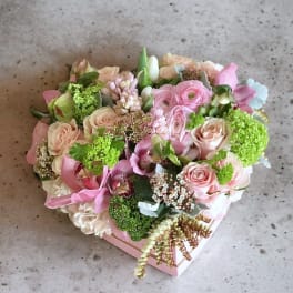 Heart-shaped box of pink and cream flowers with green accents