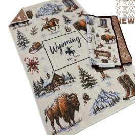 Folded Wyoming-themed towel with bison, boots, and snowy cabin illustrations
