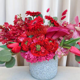 Red and pink floral arrangement in a patterned ceramic vase