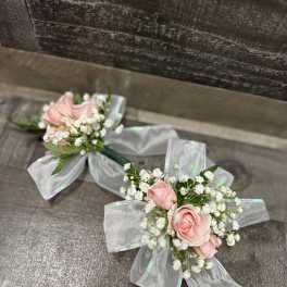 Two pink rose corsages with white baby's breath and silver ribbon bows