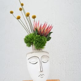 Modern floral arrangement in a white face vase with pink protea and yellow globe flowers