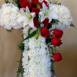 Cross-shaped floral tribute with red roses, white lilies, and white chrysanthemums
