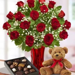 Red roses in a vase with a teddy bear and box of chocolates