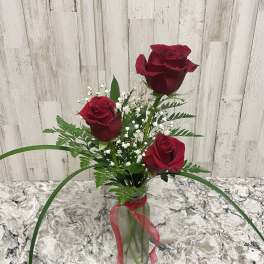 Three red roses in a glass vase with baby's breath and a red ribbon