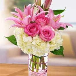 Pink lilies and roses arranged with white hydrangeas in a glass vase