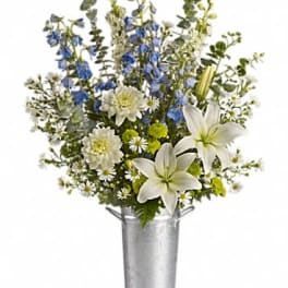 White lilies and blue flowers in a silver bucket vase