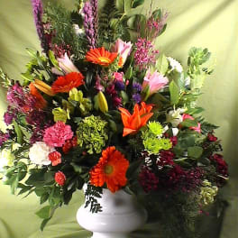 Mixed bouquet in a white pedestal vase with orange and pink blooms