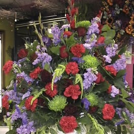 Large mixed floral arrangement in a white container with red, purple, and green blooms