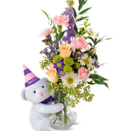 Bouquet in a glass vase with a teddy bear wearing a party hat