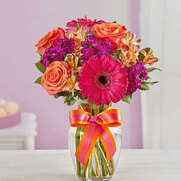 Bouquet of pink and orange flowers in a clear glass vase with a ribbon
