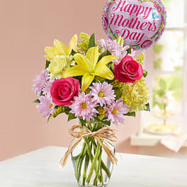 Bouquet of pink roses and yellow lilies in a glass vase with a Mother's Day balloon
