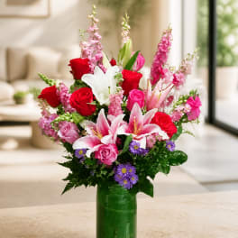 Mixed bouquet of roses, lilies, and purple daisies in a green glass vase
