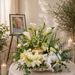White floral arrangement with calla lilies, roses, and orchids in a gold vase
