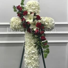 White floral cross on an easel with red roses and lilies