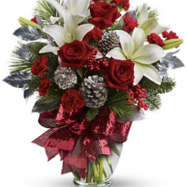 Red roses and white lilies in a glass vase with pinecones and a red ribbon