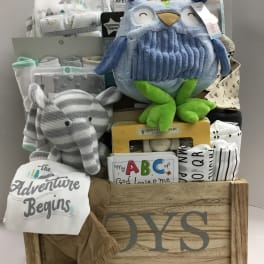 Baby gift basket with blankets, plush toys, and clothing in a wooden crate