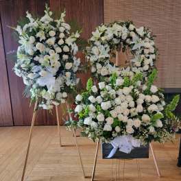 White floral funeral wreaths on stands with roses and lilies