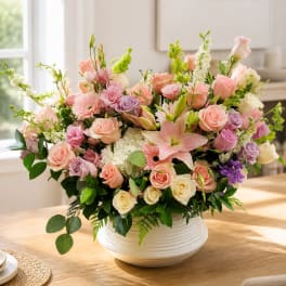 Large pastel flower arrangement in a white bowl vase on a table