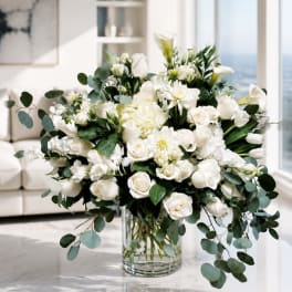 White floral arrangement in a clear glass vase with trailing eucalyptus