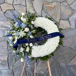 White floral wreath on an easel with blue and white flowers and a ribbon