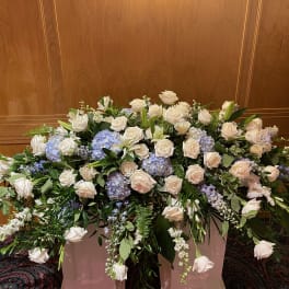Large funeral spray of white roses and blue hydrangeas in a container